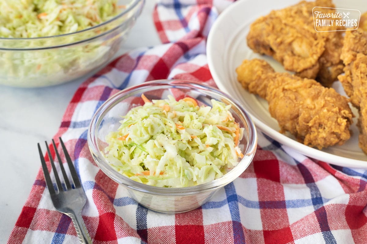 Small bowl of Coleslaw with pepper. Chicken on the side.
