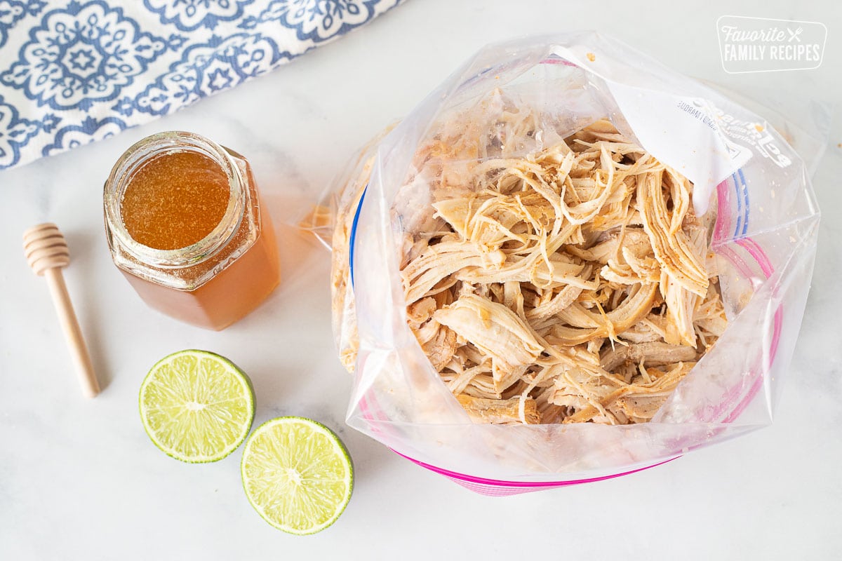 Shredded chicken in a bag next to honey and limes for Honey Lime Chicken Enchiladas.