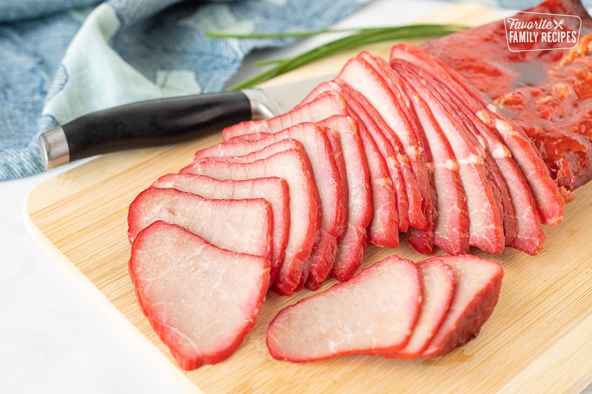Sliced Char Siu (Chinese BBQ Pork) fanned out on a cutting board with a knife.