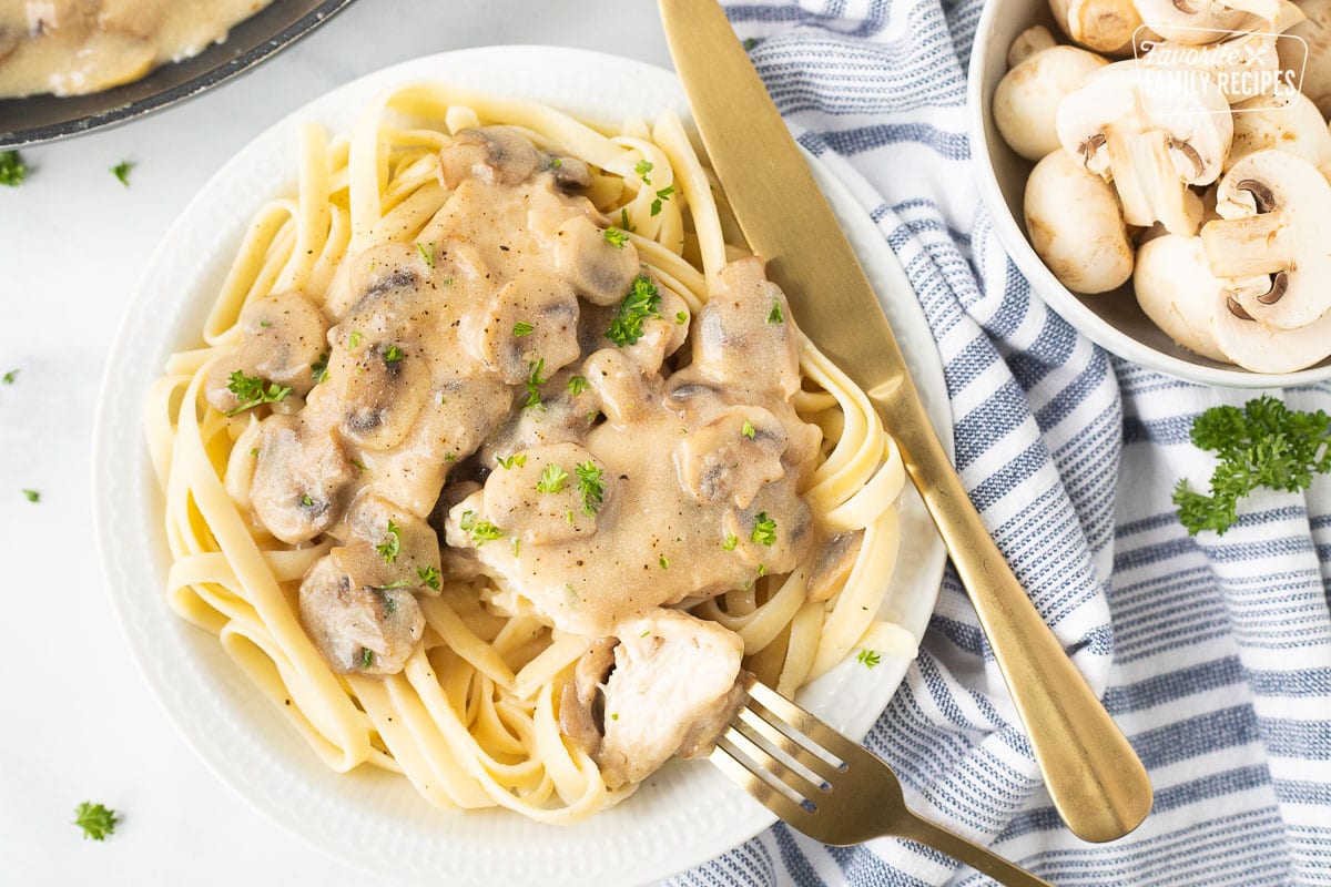 Plate with Chicken Marsala fettuccine over pasta with a knife and fork.