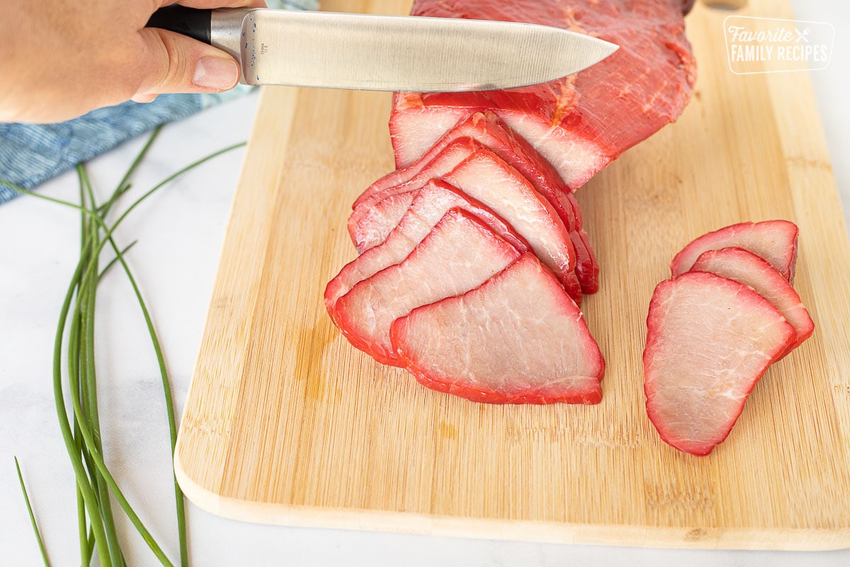 Slicing smoked Char Siu (Chinese BBQ Pork) on a cutting board.