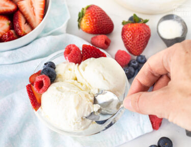 Hand scooping into a bowl of Homemade Vanilla Ice Cream with fresh berries.