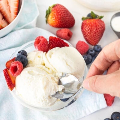 Hand scooping into a bowl of Homemade Vanilla Ice Cream with fresh berries.