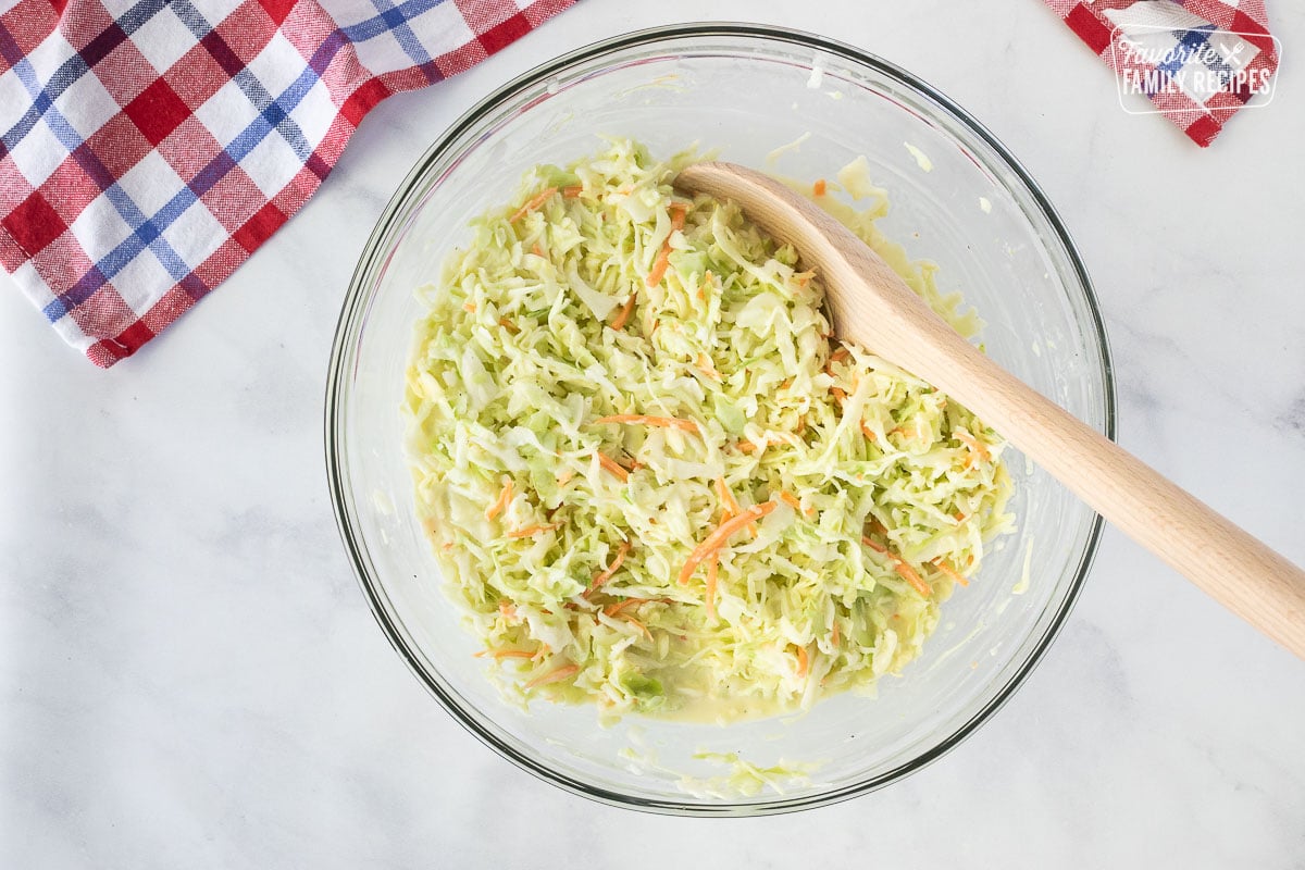 Wooden spoon mixing a bowl of cabbage, carrot and dressing for Coleslaw.