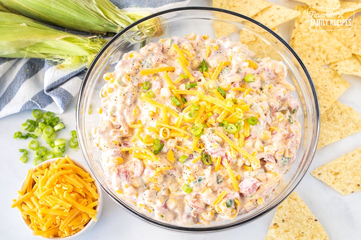 Large bowl of Creamy Corn Dip garnished with cheddar cheese and green onions.