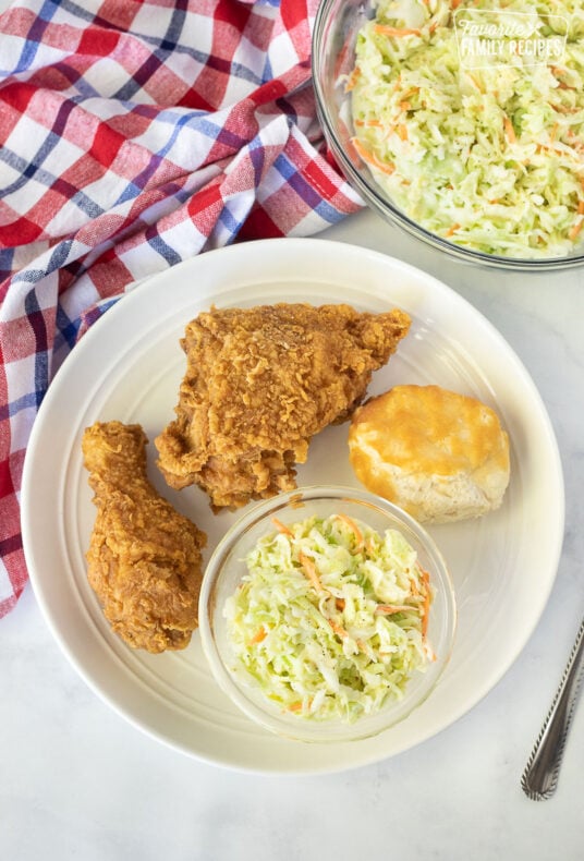 Plate of fried chicken with a biscuit and a bowl of Coleslaw.
