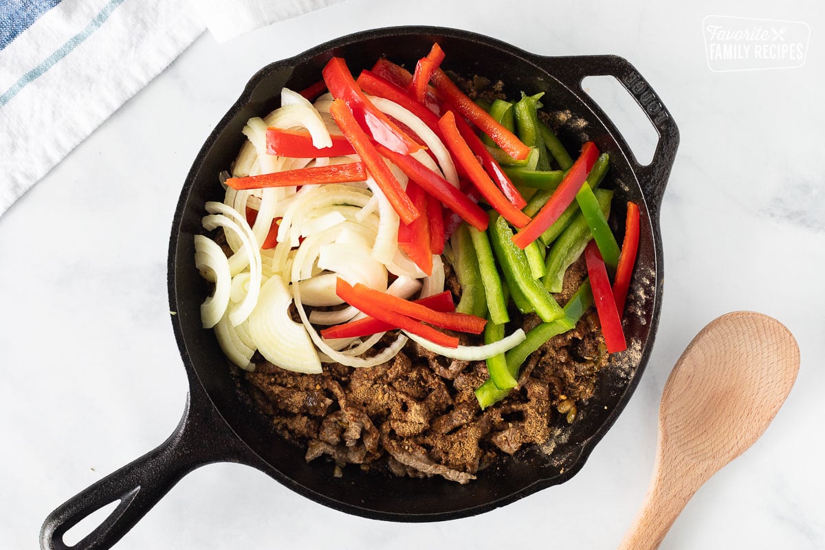 Red and green bell peppers and sliced onions added to cooked steak skillet for Steak Fajita Bowls.