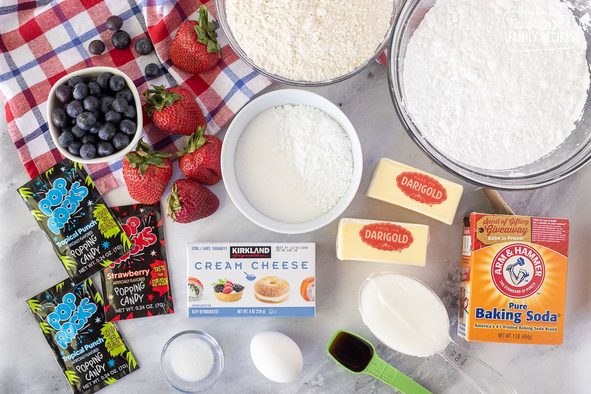 Ingredients to make 4th of July Cookies including flour, butter, sugars, baking soda, shortening, vanilla, egg, salt, cream cheese, strawberries and pop rocks.