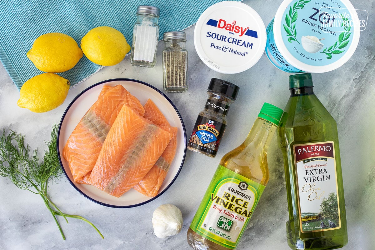 Ingredients to make Baked Lemon Salmon including sour cream, greek yogurt, salt, pepper, lemons, dill, salmon, Montreal seasoning, garlic, rice vinegar and olive oil.