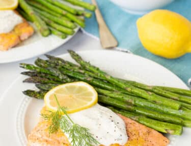Two plates of Baked Lemon Salmon with Tzatziki sauce and asparagus.