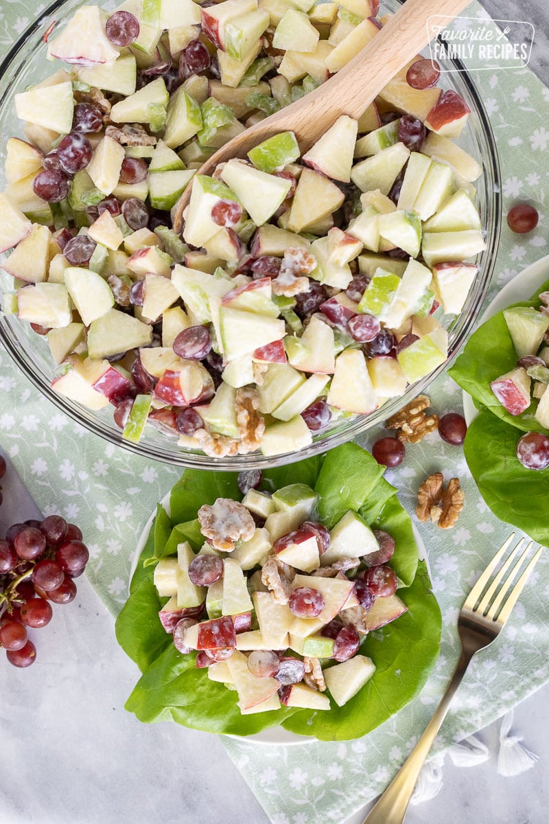 Bowl of Waldorf Salad next to plates of Waldorf Salad over green lettuce.