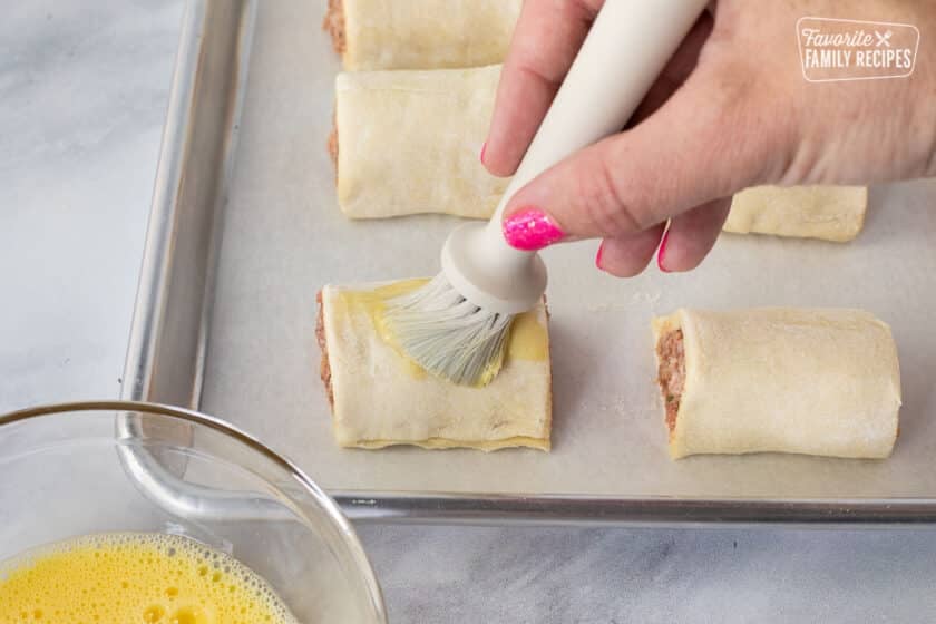 Brushing egg wash on top of a unbaked Sausage Roll.