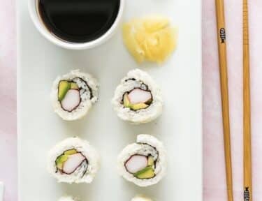 A plate of California Rolls with a cup of soy sauce and chopsticks on the side