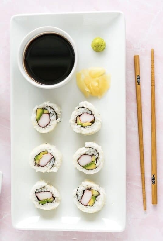 A plate of California Rolls with a cup of soy sauce and chopsticks on the side