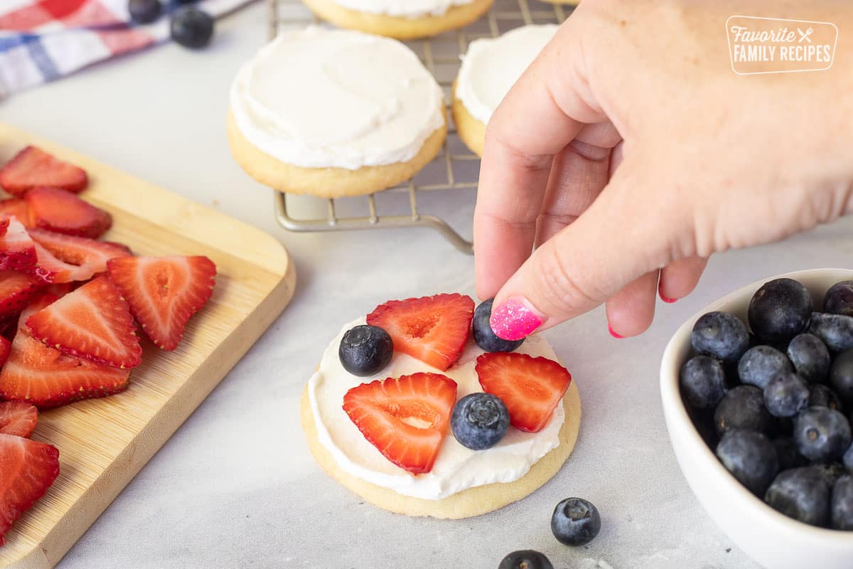 Placing fresh strawberries and blueberries on a frosted sugar cookie for 4th of July Cookies.