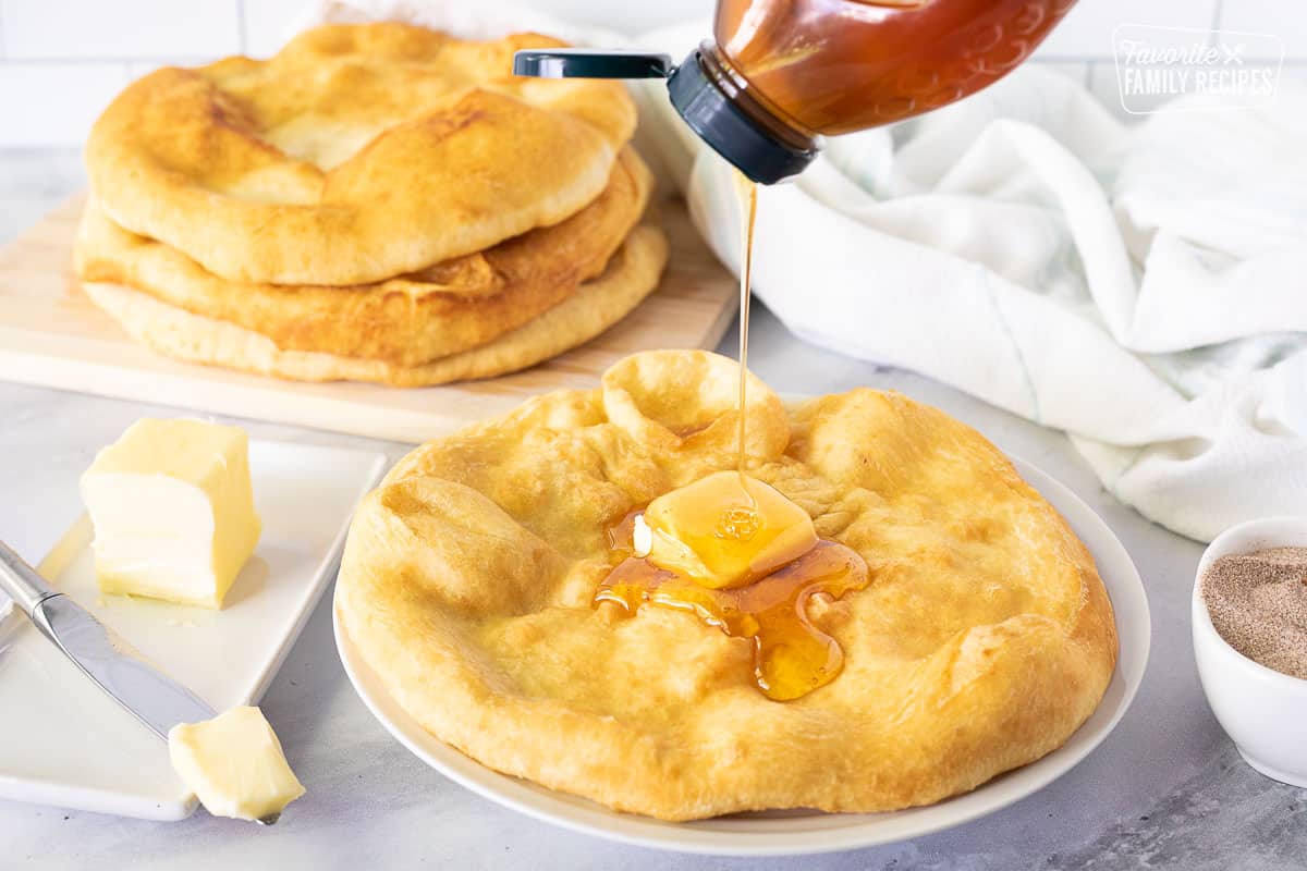 Pouring honey on a piece of Fry Bread with butter.
