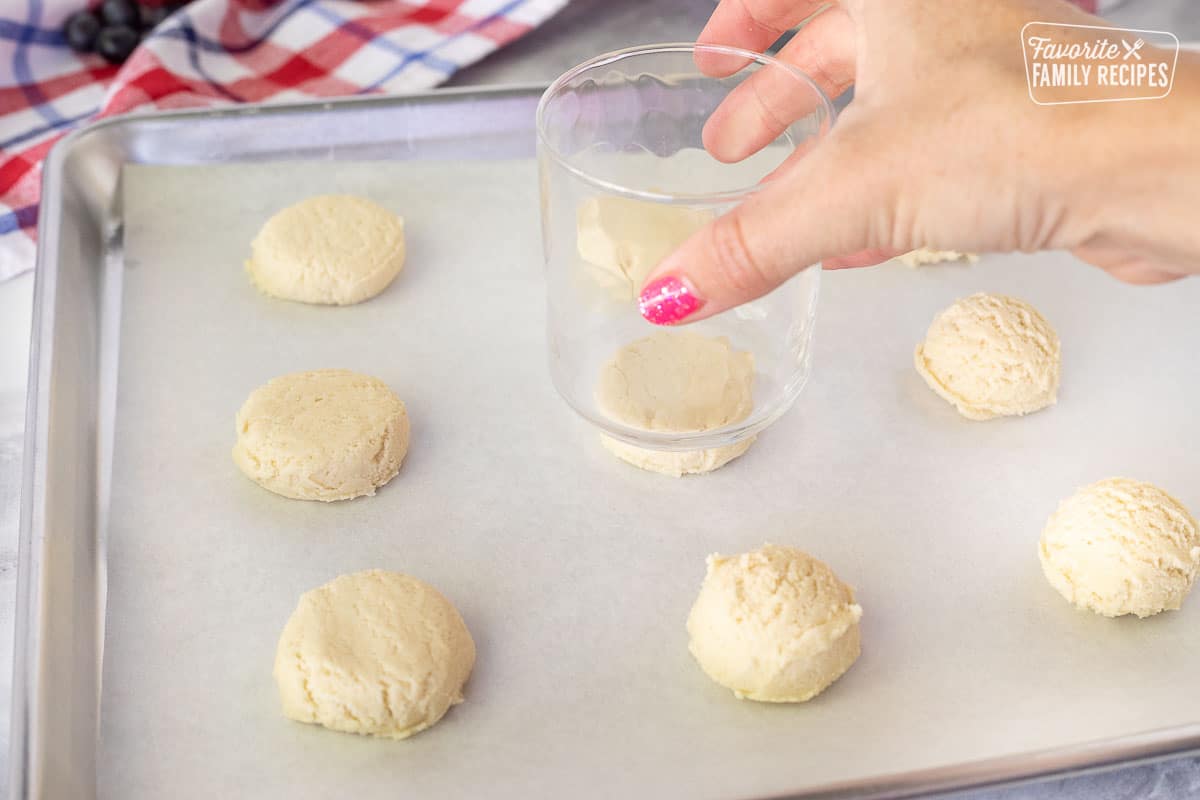 Hand holding a glass pressing down the tops of the cookie dough balls for 4th of July Cookies.