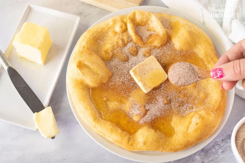 Sprinkling cinnamon sugar on a piece of Fry Bread with butter and honey.