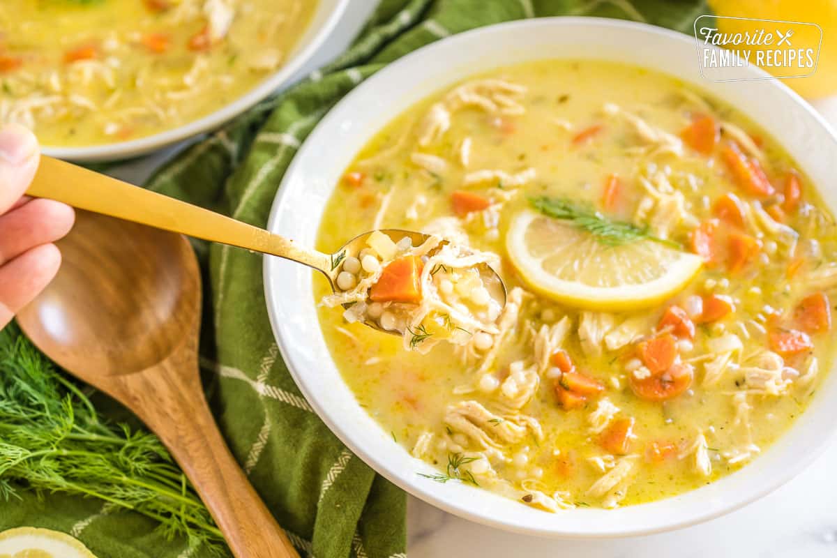 A bowl of Greek Lemon Chicken Soup topped with a lemon slice and fresh dill with a spoonful taken out.