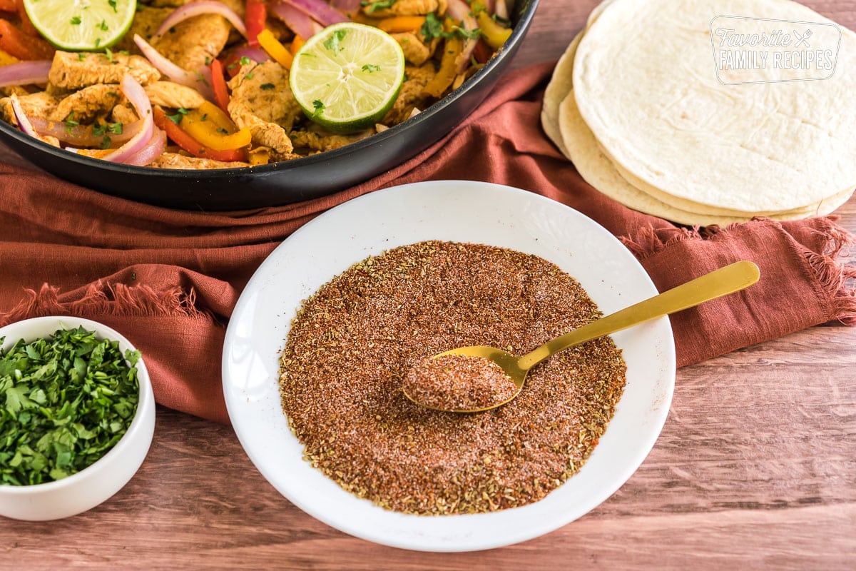 homemade fajita seasoning on a plate next to a pan of chicken fajitas