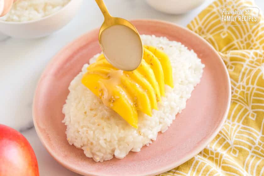Mango Sticky Rice on a pink plate with sauce being poured over the top
