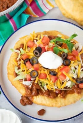 Navajo Taco on a plate with lettuce, cheese, tomatoes, olives and sour cream.