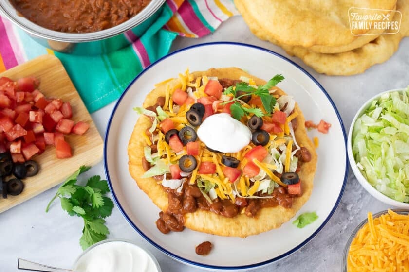 Navajo Taco on a plate with lettuce, cheese, tomatoes, olives and sour cream.