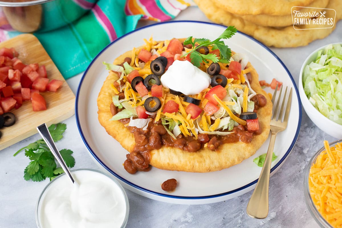Plate with a Navajo Taco topped with chili, lettuce, cheese, tomatoes, olives and sour cream.