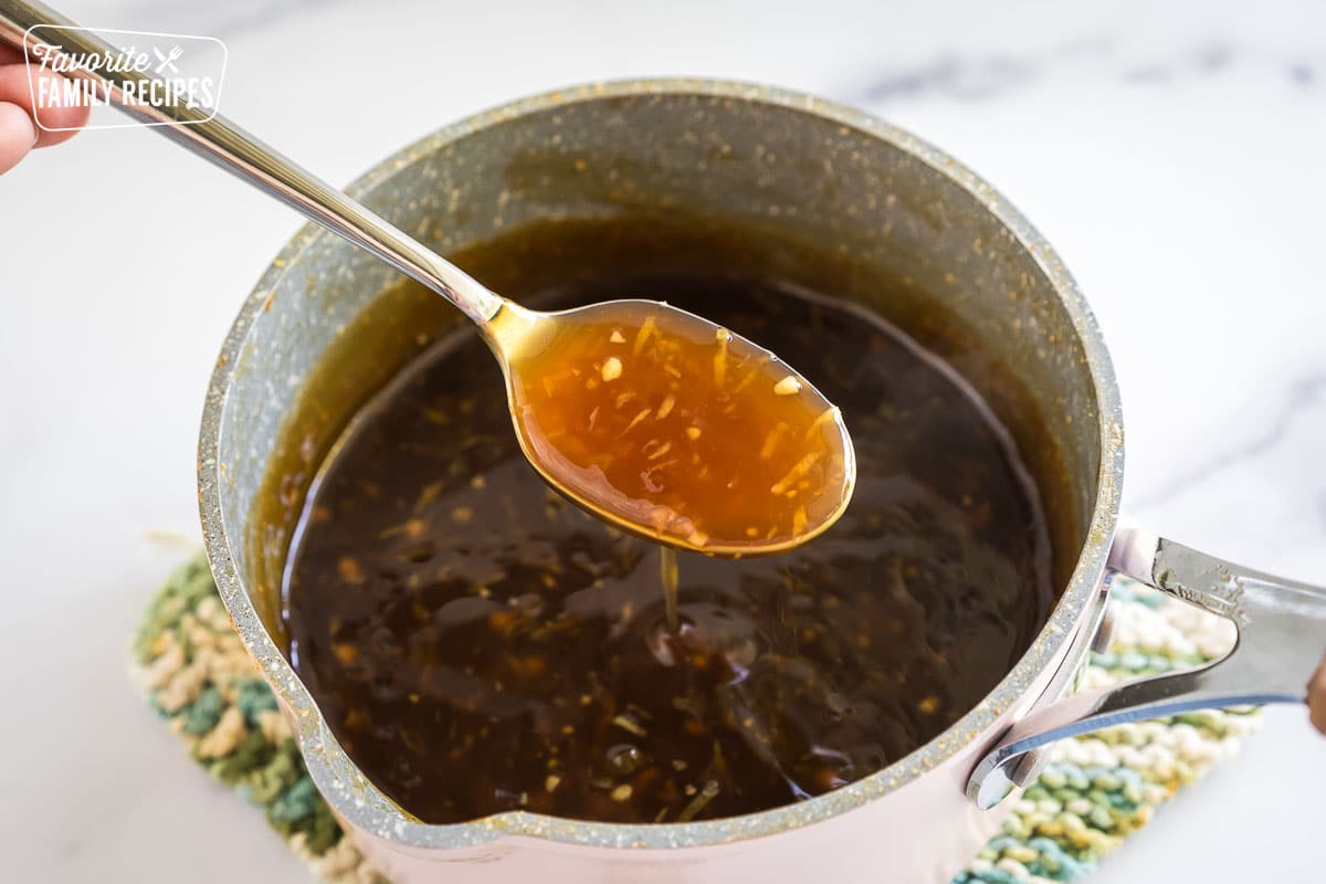 A spoonful of brownish orange sauce from a saucepan