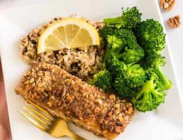 Pecan Crusted Salmon on a plate with wild rice, broccoli, and a lemon slice