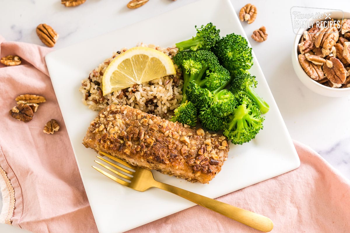 Pecan Crusted Salmon on a plate with wild rice, broccoli, and a lemon slice