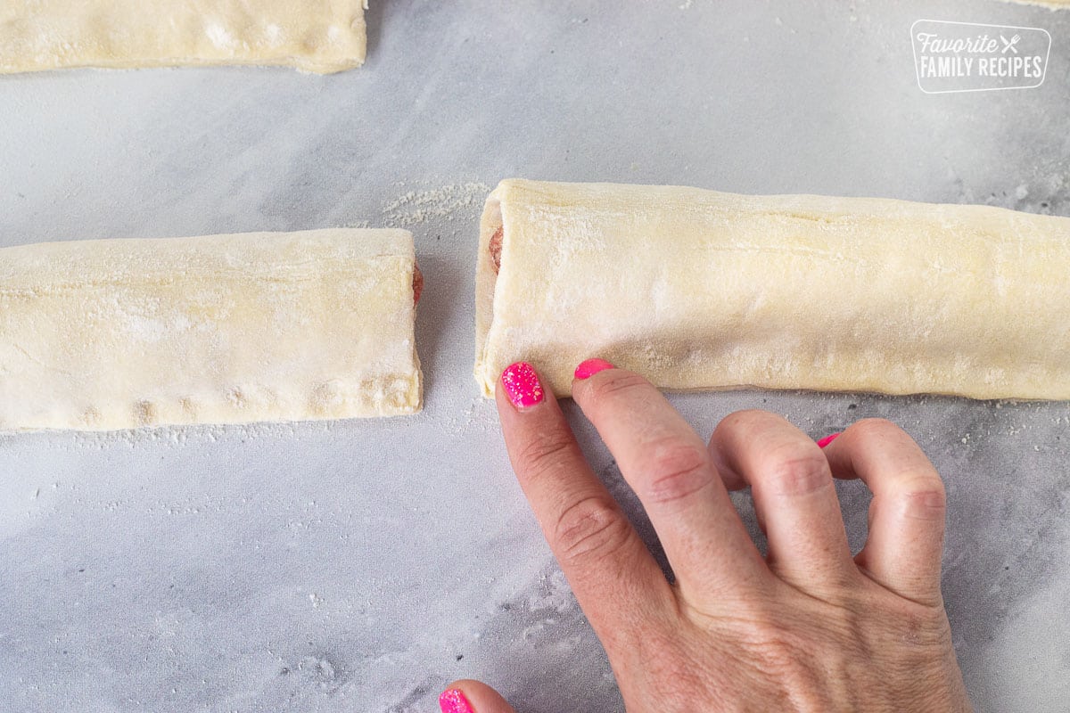 Hand pinching the edges of the Sausage Rolls.