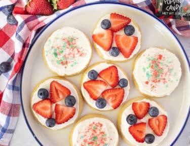 4th of July Cookies decorated with strawberries, blueberries and Pop Rocks on a plate.