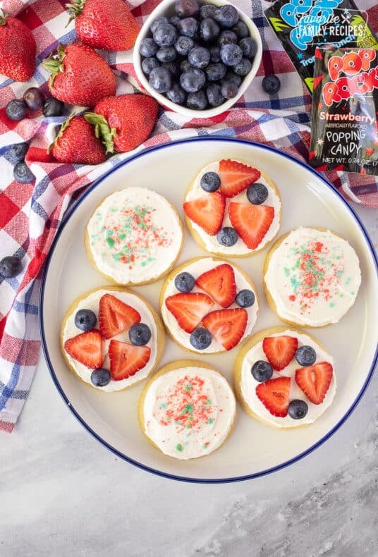 4th of July Cookies decorated with strawberries, blueberries and Pop Rocks on a plate.