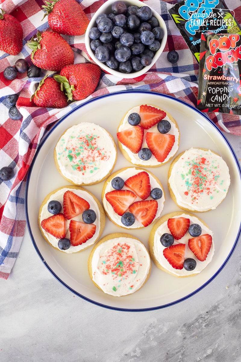 4th of July Cookies decorated with strawberries, blueberries and Pop Rocks on a plate.