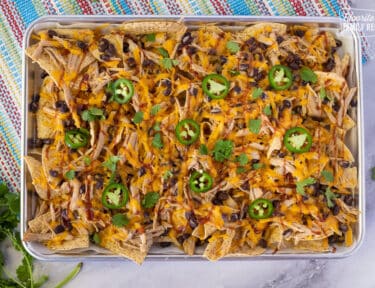 Baking sheet with Pulled Pork Nachos topped with BBQ sauce, cilantro and sliced jalapeños.