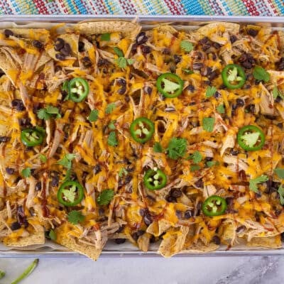 Baking sheet with Pulled Pork Nachos topped with BBQ sauce, cilantro and sliced jalapeños.