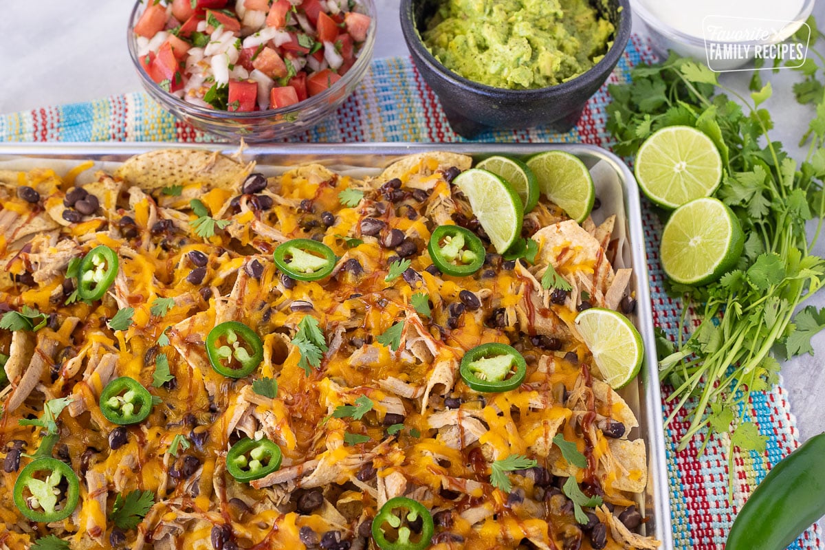 Side view of Pulled Pork Nachos in a baking dish with pico and guacamole on the side.