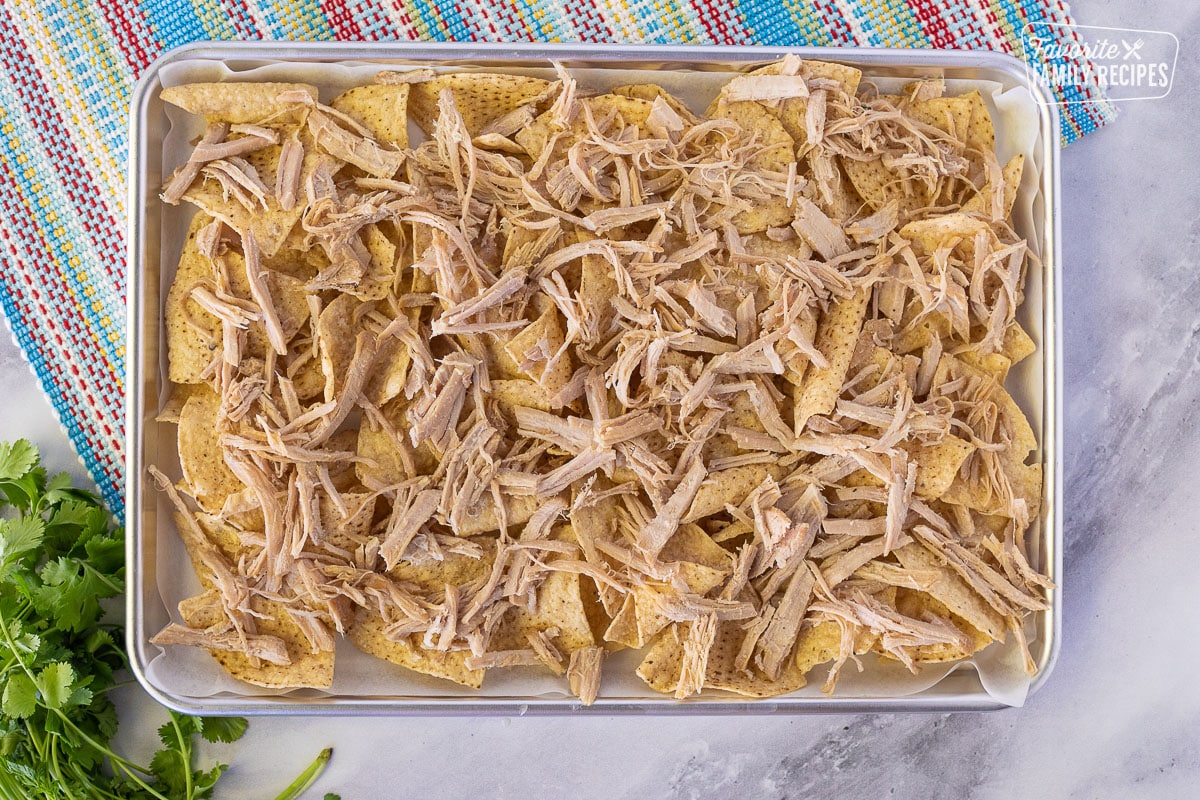 Baking sheet of tortilla chips topped with Pulled Pork for Nachos.