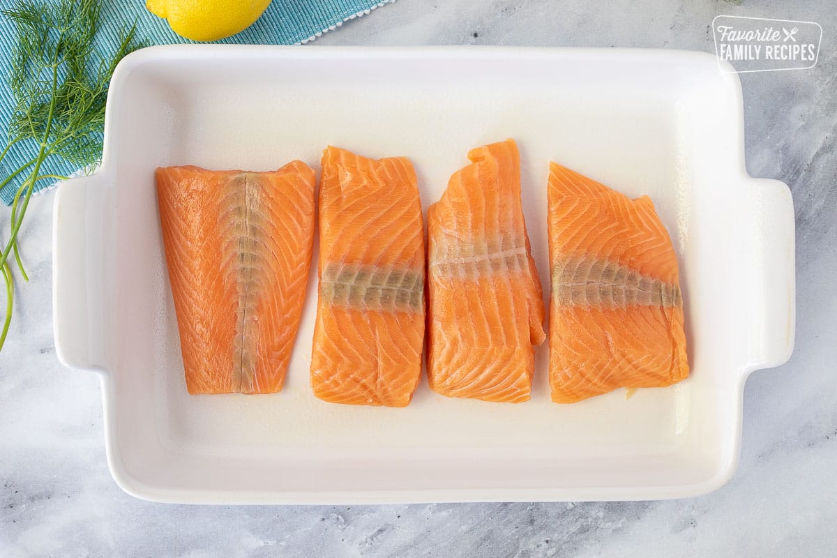 Baking dish with four salmon fillets for Baked Lemon Salmon.
