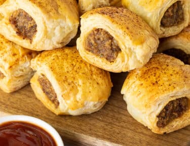 Baked Sausage Rolls on a board next to a small bowl of ketchup.