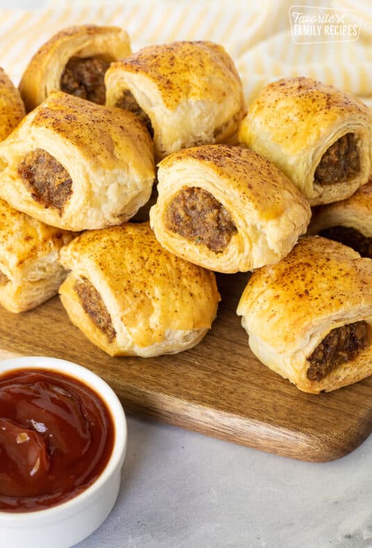 Baked Sausage Rolls on a board next to a small bowl of ketchup.