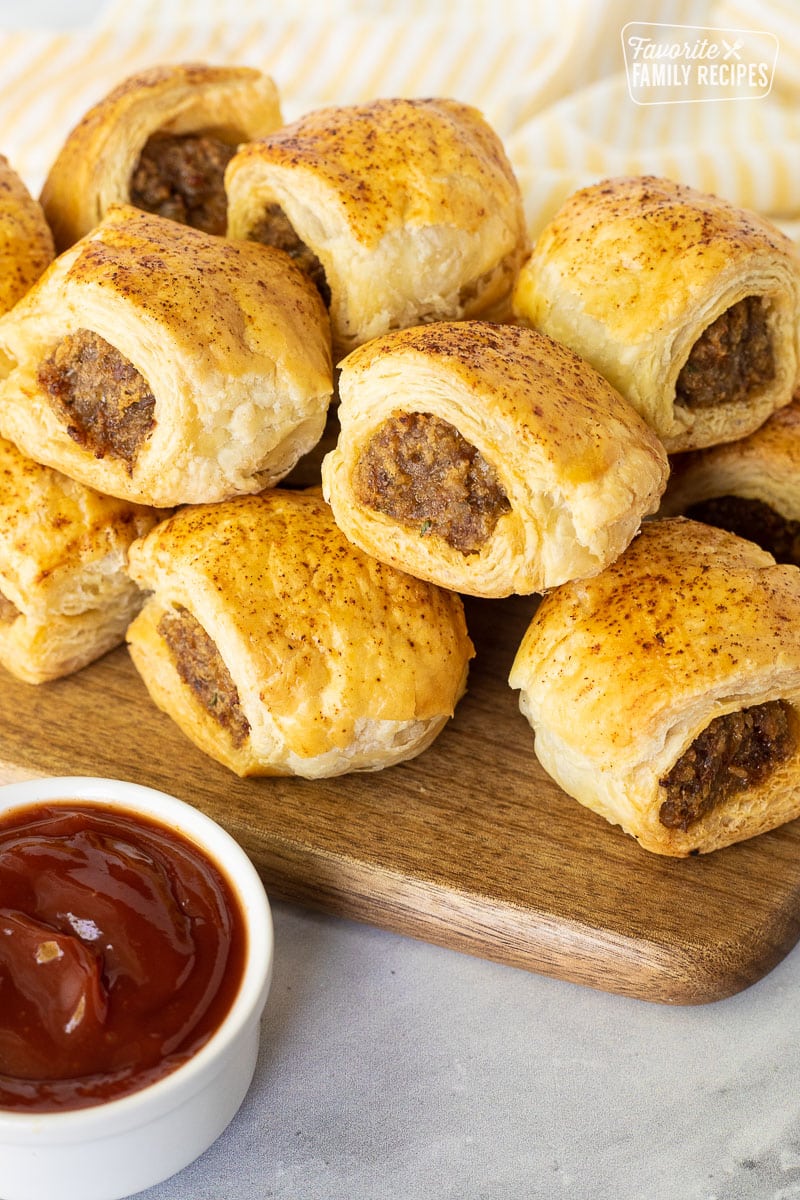 Baked Sausage Rolls on a board next to a small bowl of ketchup.