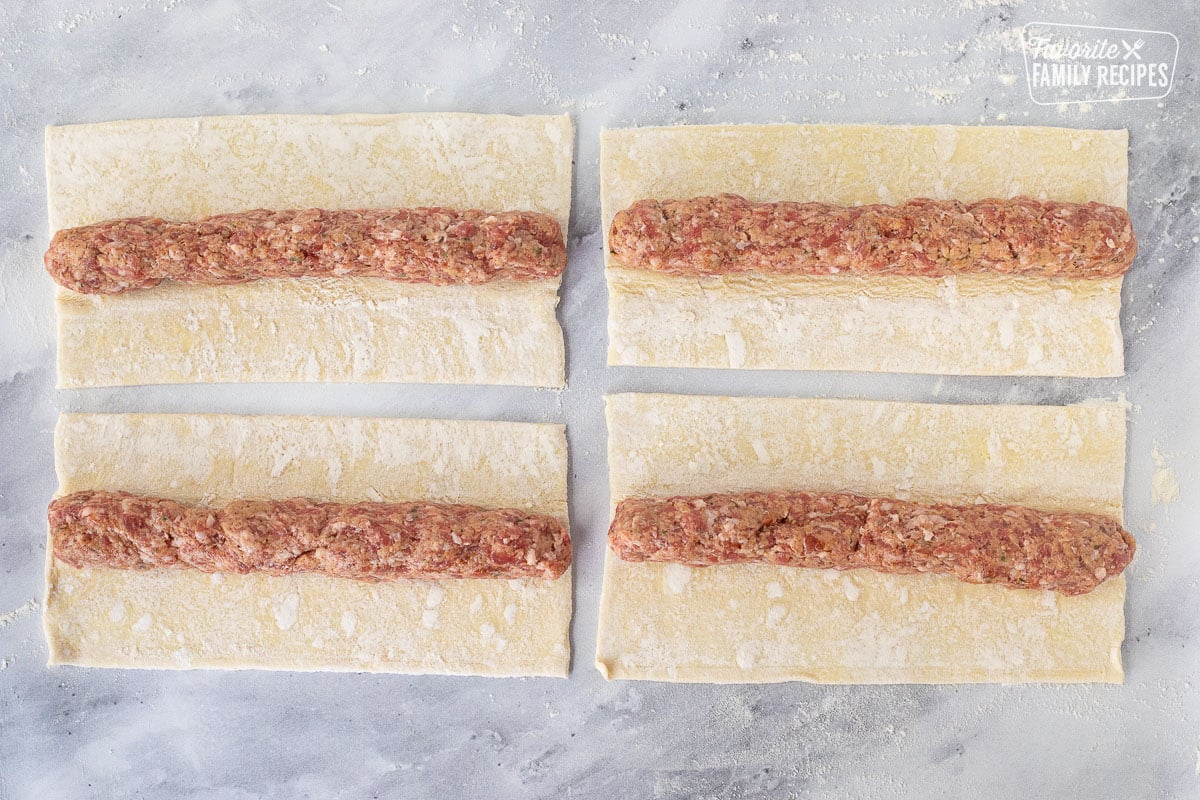 Rolled logs of sausage mixture on top of the four rectangle puff pastry sheets.
