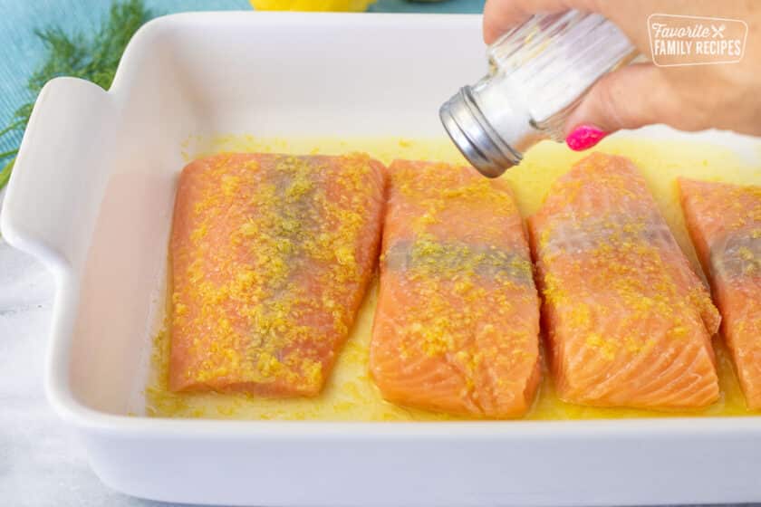 Shaking salt onto fillets of salmon in a baking dish for Baked Lemon Salmon.