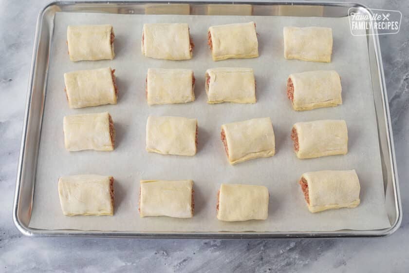 Baking sheet with parchment paper with sixteen cut Sausage Rolls.