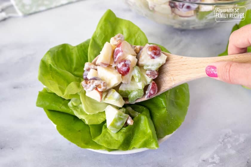 Hand holding a wooden spoon placing Waldorf Salad on top of lettuce greens.