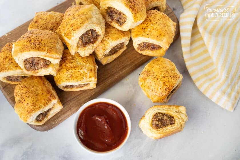 Top view of Sausage Rolls on a board next to a bowl of ketchup.