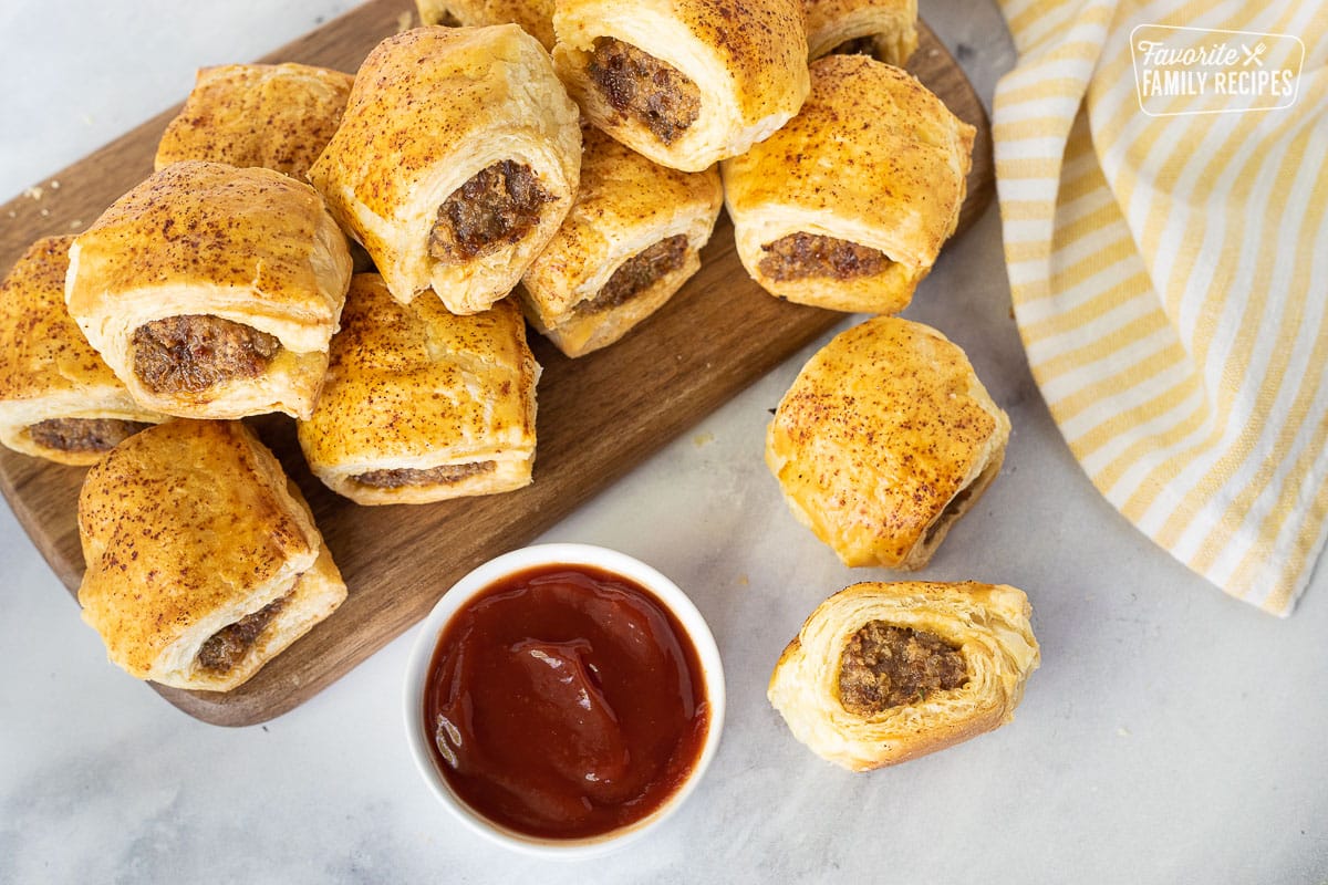 Top view of Sausage Rolls on a board next to a bowl of ketchup.
