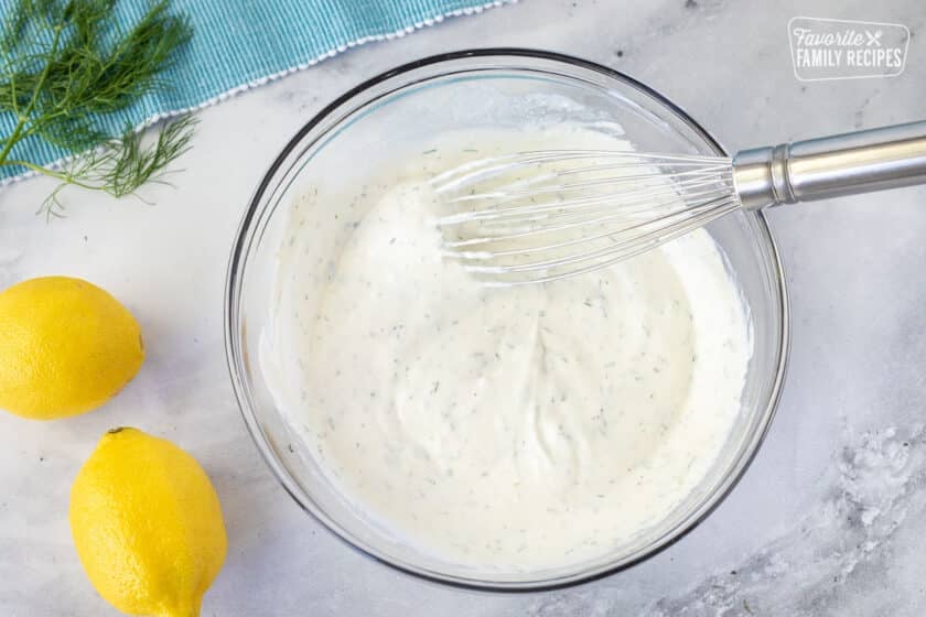Glass bowl of Tzatziki sauce for Baked Lemon Salmon with a whisk.